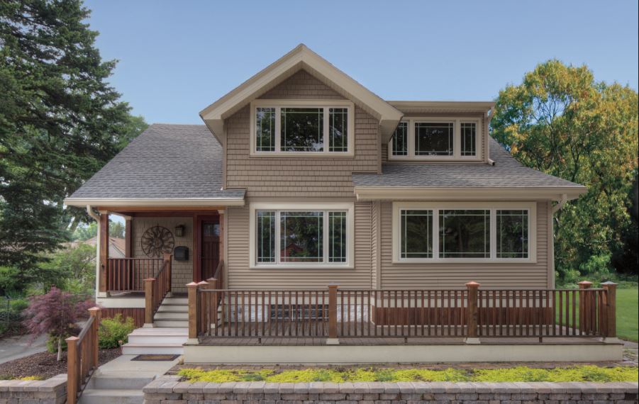 Two-story home with tan shingle siding and sets of white casement windows.