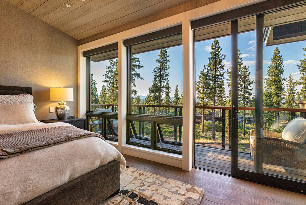 Sliding patio door in a bedroom, leading onto a deck with view of pine trees.