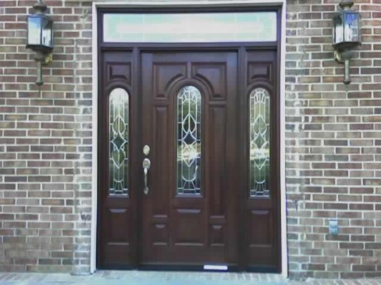 Dark wood-grain front door with decorative glass and decorative matching sidelites in a brick home.