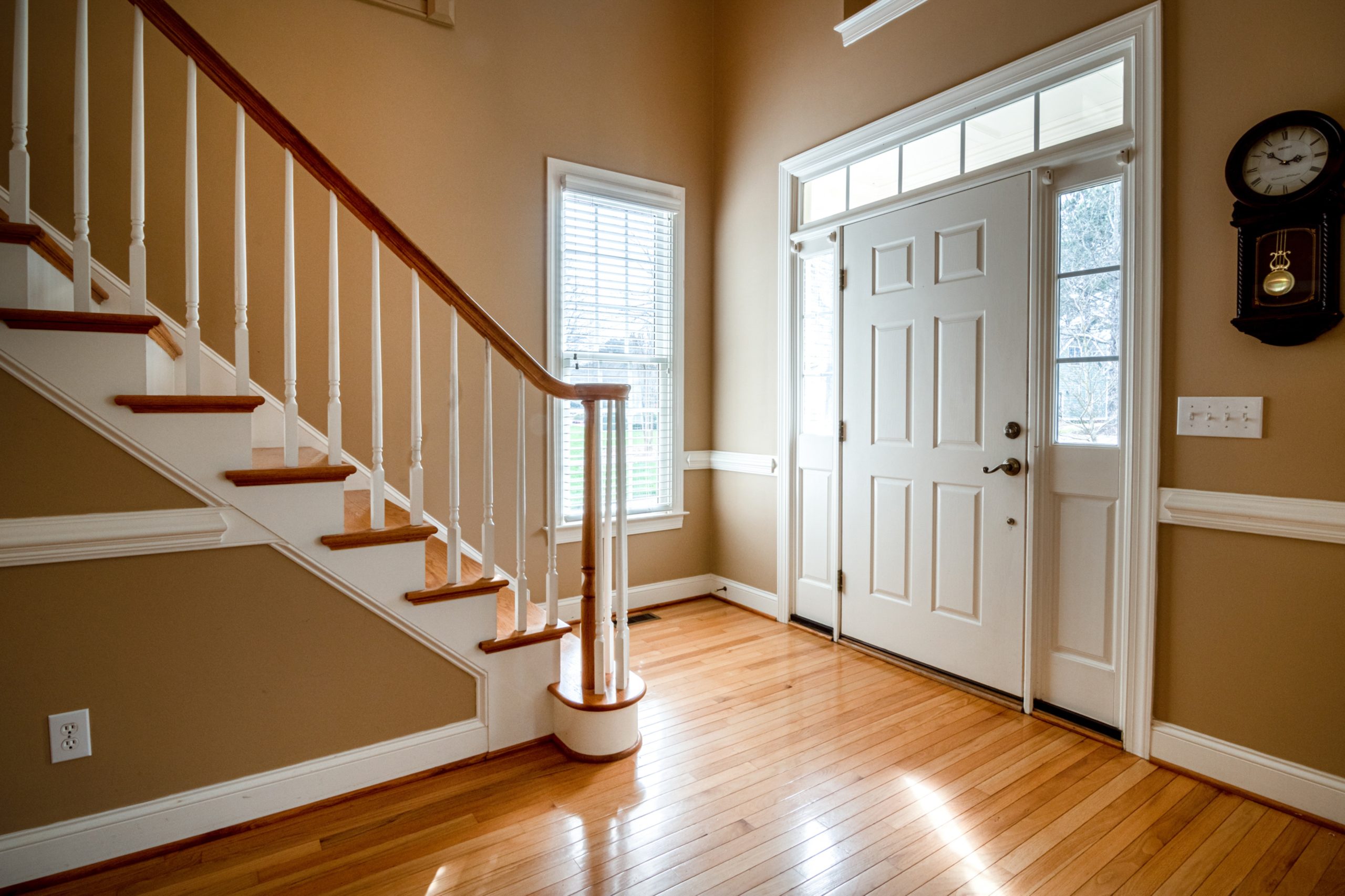 Interior view of home entryway with a wooden staircase leading to an energy-efficient white entry door with sidelites..