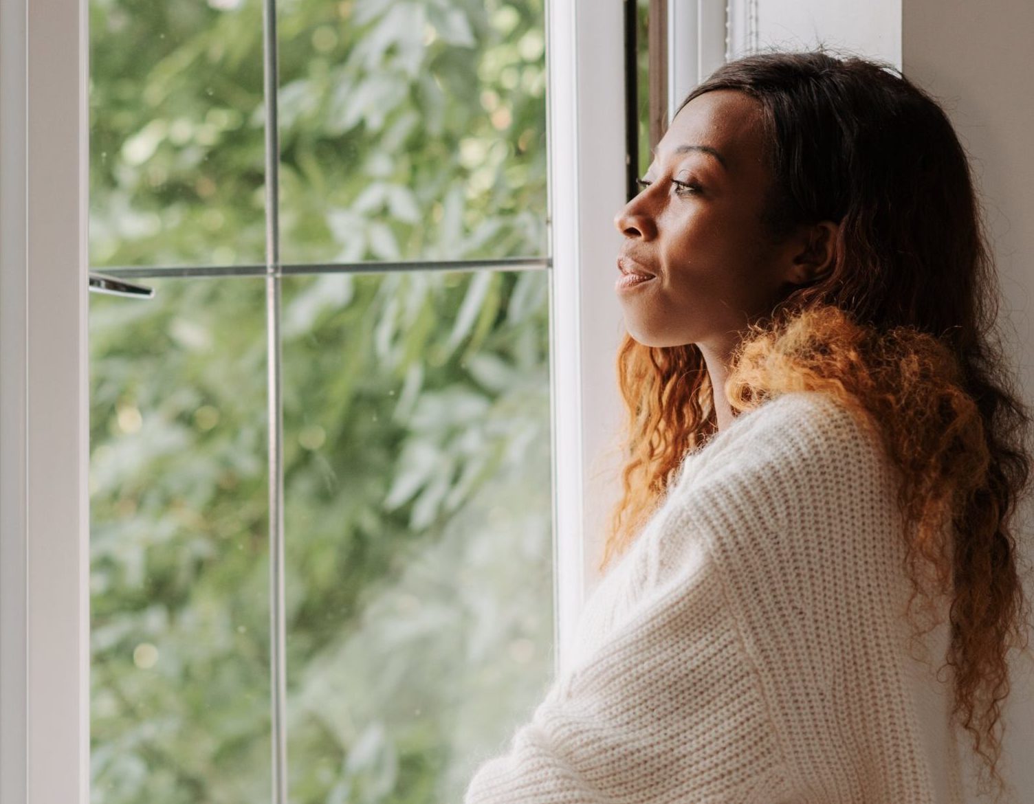 Woman wearing a white sweater and looking out an open window.
