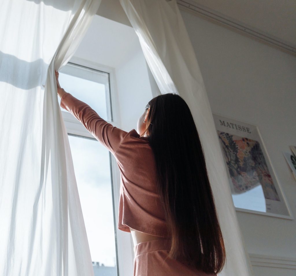 Young woman opening white curtains in front of a new window.