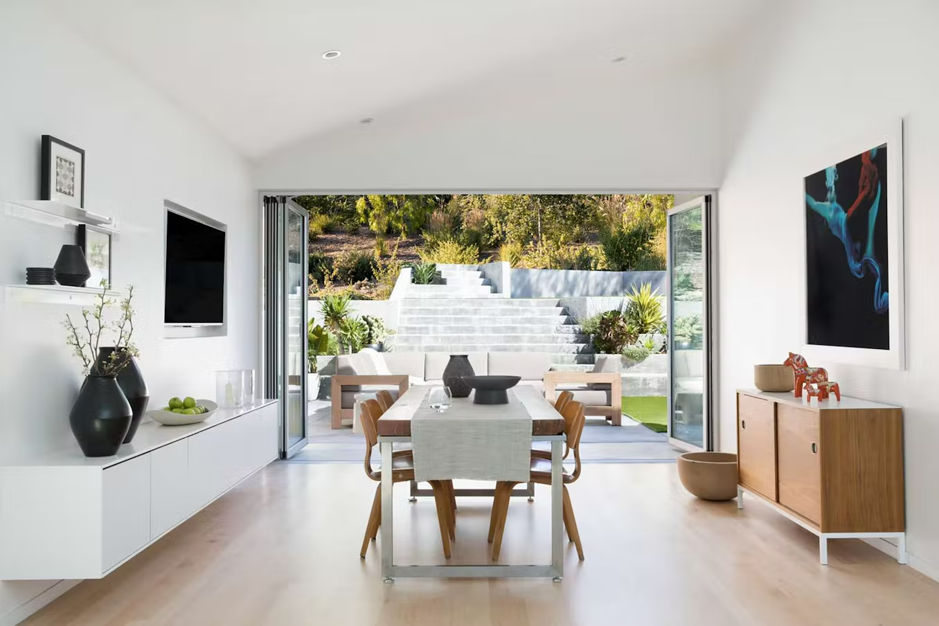 Open glass patio doors leading from a bright, modern dining area to a well-manicured backyard with patio.