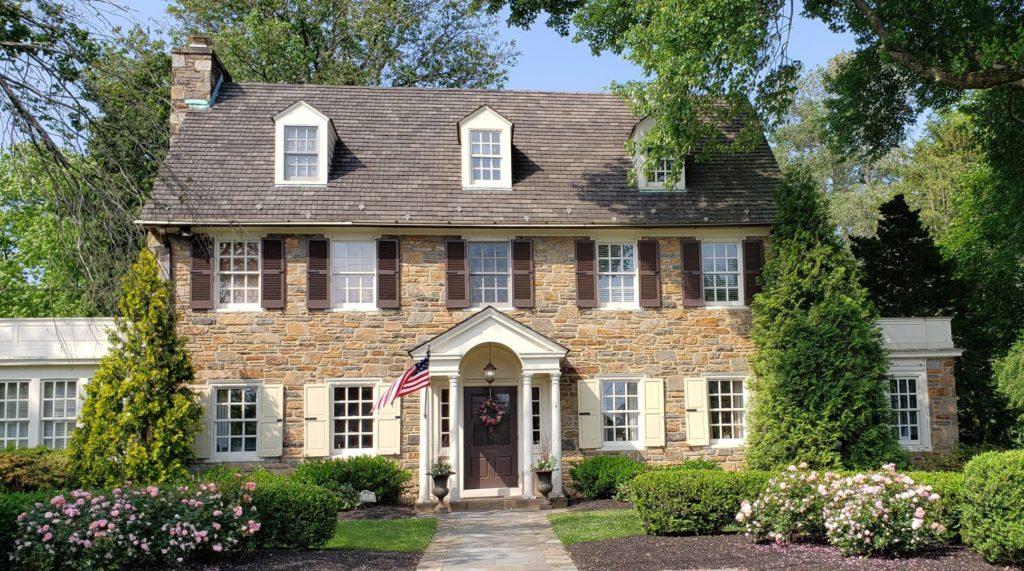 Historic stone colonial-style home near Potomac, MD. Landscaped front lawn and trees surrounding.